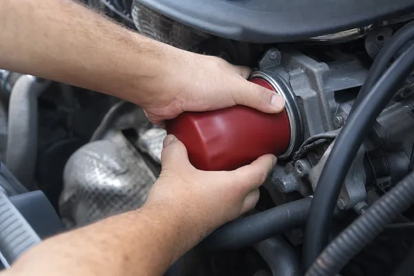 Hands screwing a red spin-on oil filter onto the engine by hand