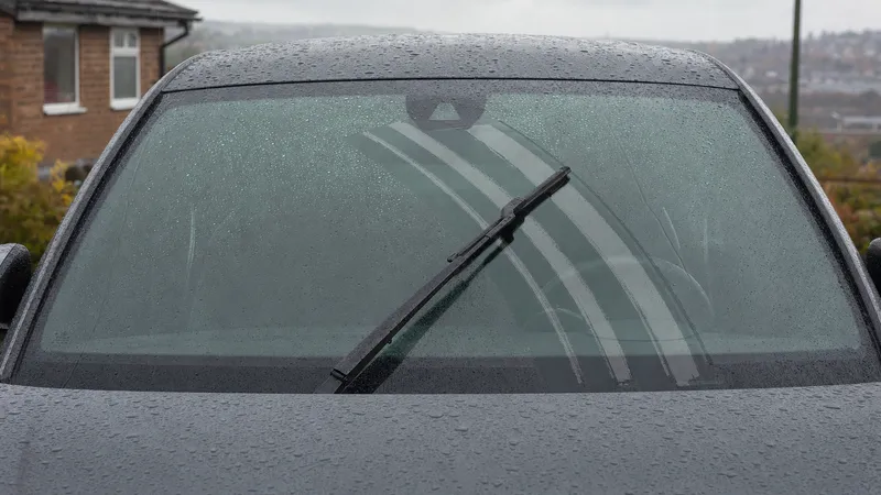 A wiper blade halfway through its sweep on a rainy windscreen, leaving bands of water behind it